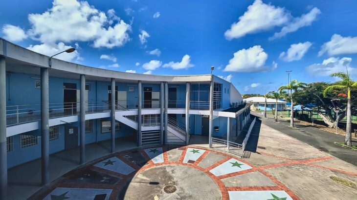 Cour centrale du collège Eugène Yssap avec son sol décoré d'étoiles et le bâtiment bleu à deux niveaux sous un ciel dégagé