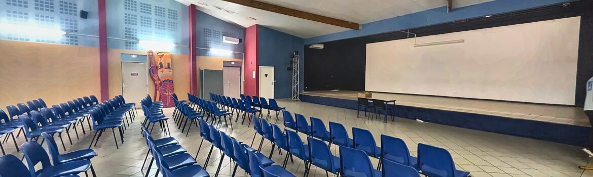 Salle polyvalente du collège avec des rangées de chaises bleues face à la scène