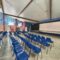 Salle polyvalente du collège avec des rangées de chaises bleues face à la scène