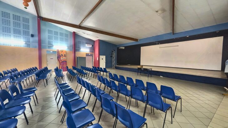Salle polyvalente du collège avec des rangées de chaises bleues face à la scène